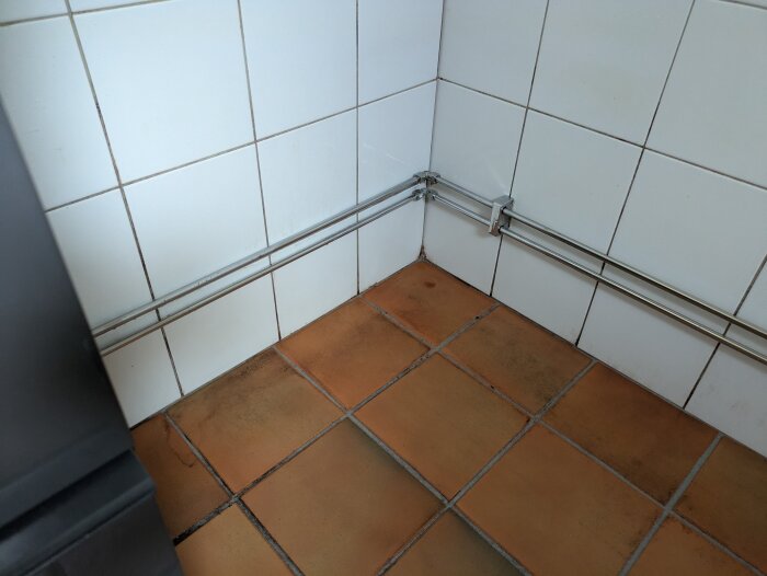Smuts och svartmögel bakom ett borttaget badkar, med vita kakelplattor och orangefärgade golvplattor.