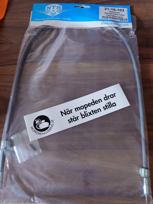 Förpackning med en hastighetsmätarkabel från NTS på ett bord, med en logotyp och texten "När mopeden drar står blixten stilla".
