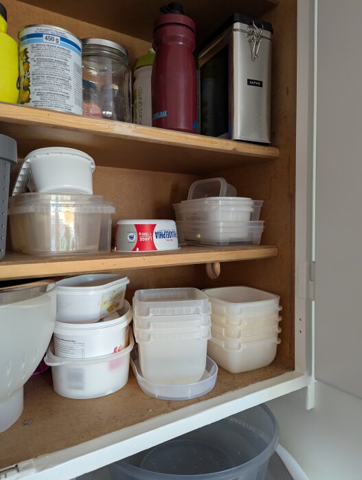 Öppet köksskåp med plastbehållare, matburkar, en röd vattenflaska och en metallburk märkta "KAFFE".