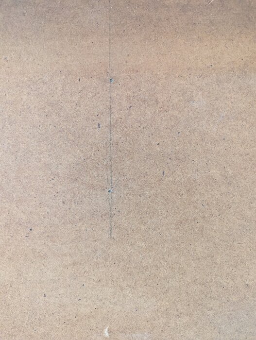 Närbild av en träpanel med ett smalt spår och en synlig spik i mitten som används för att fästa skåpet i köket.