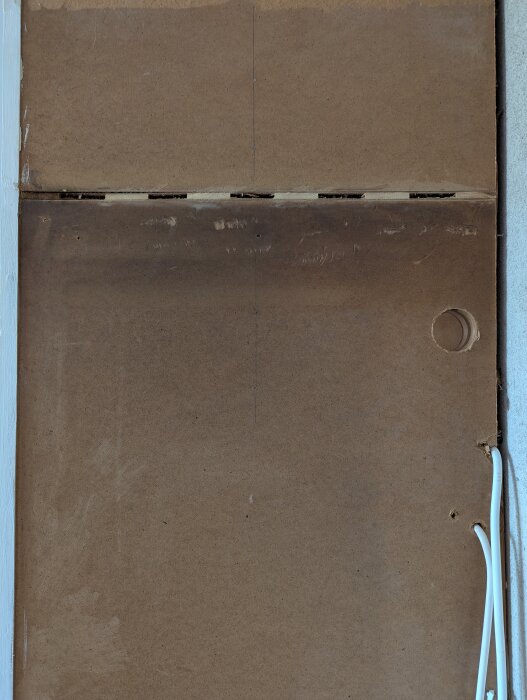 Närbild på baksidan av ett köksskåp med en träpanel och en vit sladd längs höger kant.