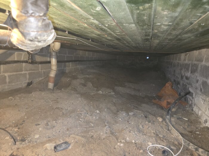 Krypgrund under hus med ojämn jord, rör och byggmaterial.