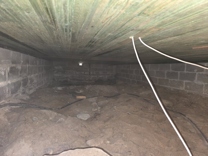 Krypgrund med ojämn jord och synliga kablar under ett trägolv, redo för utjämning.