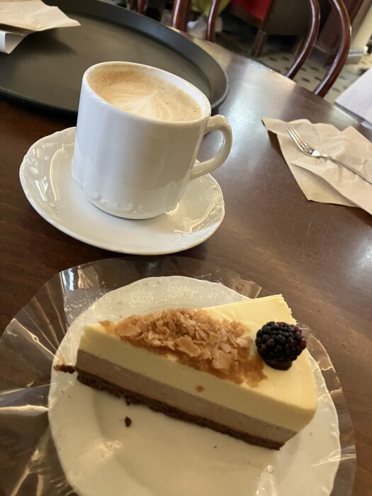 Kaffe med latte art och en tårtbit med choklad och bär på ett kafébord.