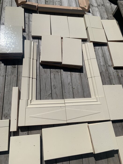 Vita kakelplattor och lister placerade på ett trädäck, förmodligen till en combitherm-kamininstallation.