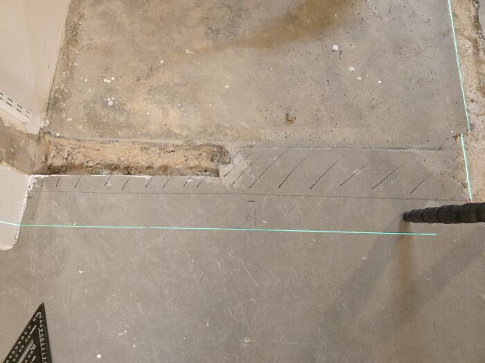 Betonggolv med markerade streck för rivning och golvjustering, linjerade med laser för planering av väggflyttning i förråd och korridor.