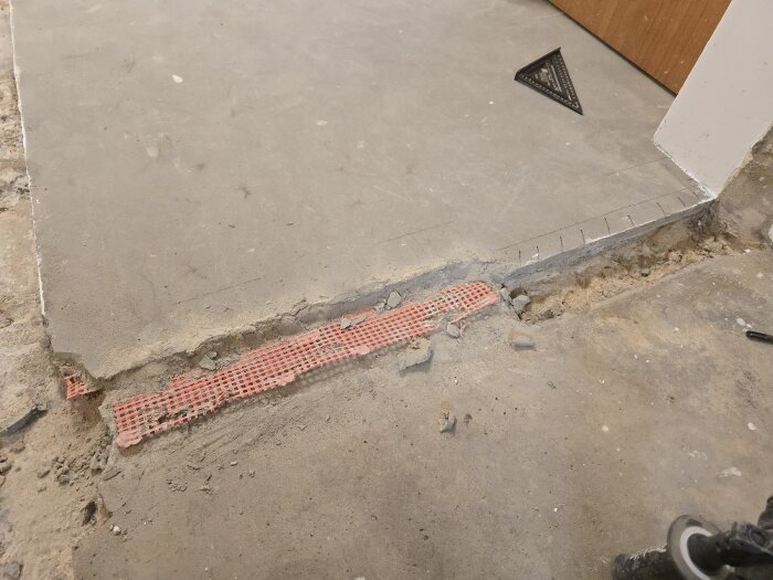 Knackat betonggolv med synlig glasfiberarmering och streckade markeringar för borttagning nära en dörröppning.
