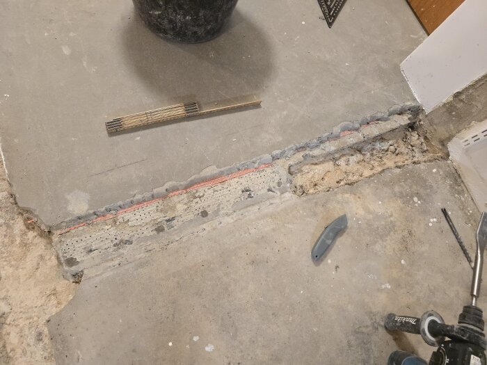 Betonggolv med ränna, markerad med röda streck för byggprojekt; inkluderar verktyg som skärare, måttstock och borrhammare på golvet.