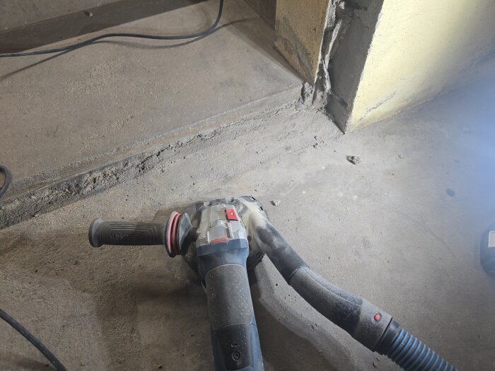 Betonggolv med en ränna och en vinkelslipmaskin, förberett för arbete med att jämna ytan vid en vägg.