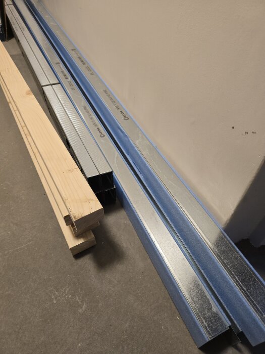 Plåtreglar och träreglar staplade på golvet, redo för användning i byggprojektet. Reglarna ligger i ett lager trefärgade och obehandlade.