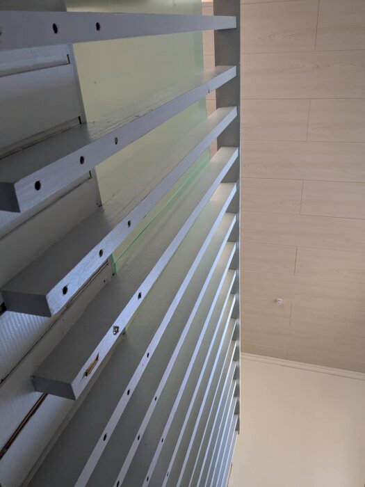 Kældersituation med delvist fjernet rækværk; planhyvlade fyrplanker monteret vertikalt til en væg med synlige skruehuller og grøn overflade bagved.