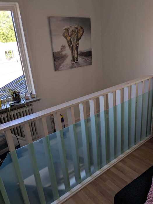 Kælderrækværk med grønne glasplader og trælister under elefantmaleri på væg i lys stue.