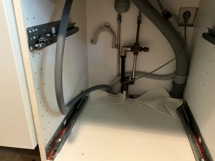 Diskmaskinens avloppsinstallation med synliga rör och slangar under ett köksskåp, inga tecken på skada eller blockering.