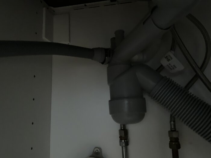 Diskmaskinsavloppsslangar under diskbänken med anslutningar och krökta rör som undersöks för potentiellt stopp.