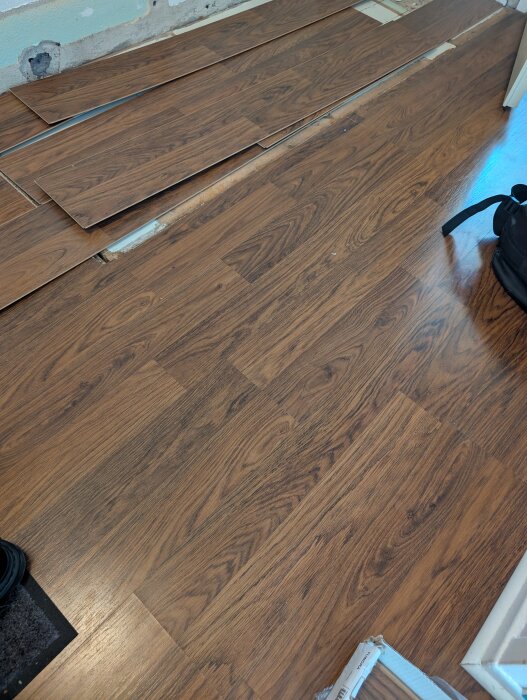 Trägolv av mörk ek med IKEA Tundra-paneler, ofärdigt projekt där skivor saknas.