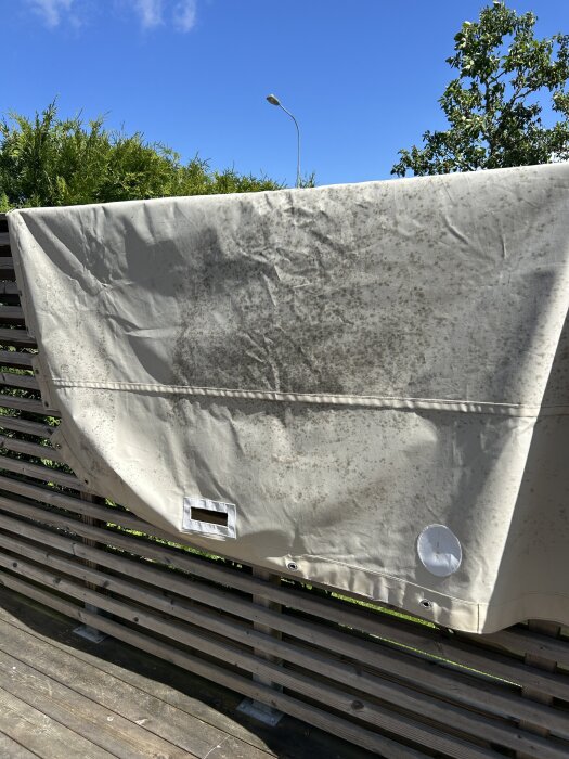 Båtkapell hänger på ett staket, visar stora mörka fläckar av mögel på tyget under en klarblå himmel.