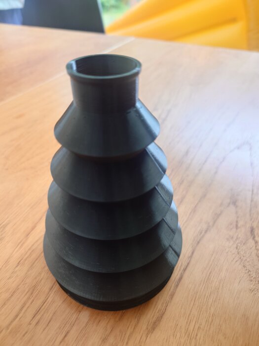 3D-utskriven svart TPU-bälg på träbord, flerradig design.