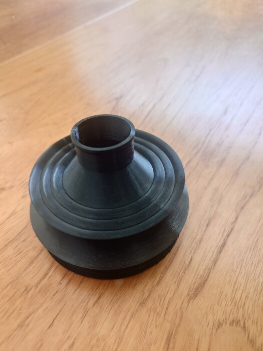 3D-utskriven svart bälg av TPU-material på ett trägolv, används i mekaniska sammanhang.