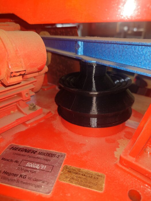 3D-utskriven bälg i TPU installerad i en Hegner-maskin, modell från 1991, med märkplåt synlig. Maskinen är delvis orange och detaljer blå.