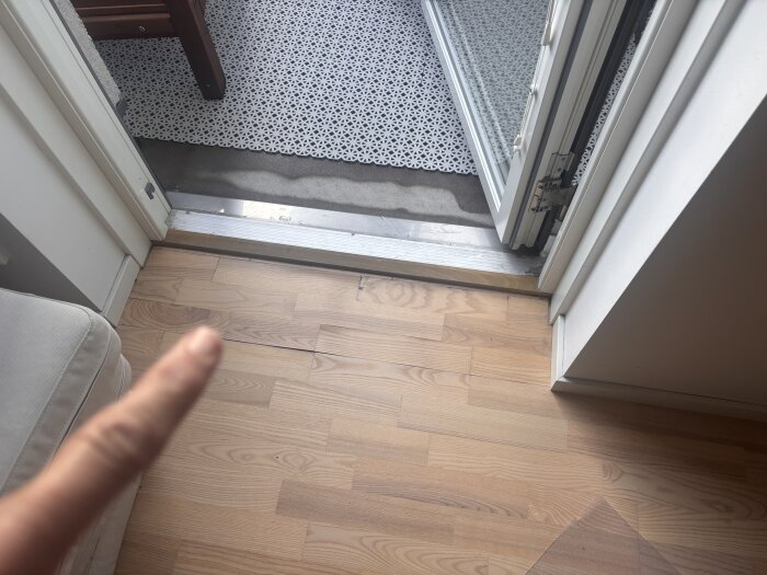 Öppen altandörr med uppstickande brädor i trägolv, finger pekar på brädor.