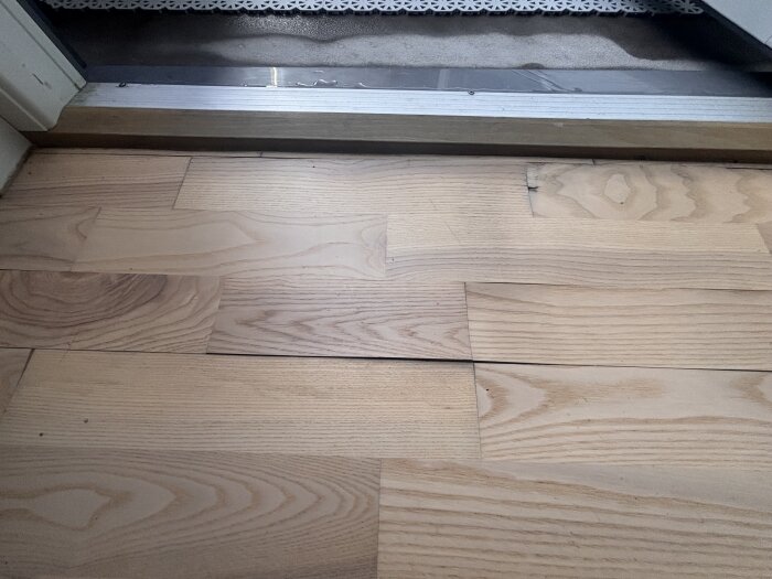 Trägolv med lätt upphöjda plankor nära en altandörr, indikerande potentiella fuktskador efter regn.