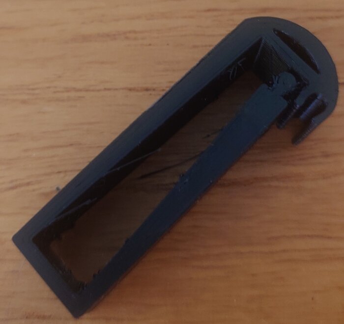 Svart plastdel, delvis egen design, som fungerar som skydd mellan dörr och räcke, placerad på en träyta.