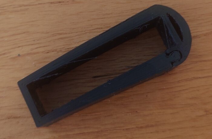 Svart, rektangulär plastdel på träyta, används som skydd mellan dörr och räcke, egen design.