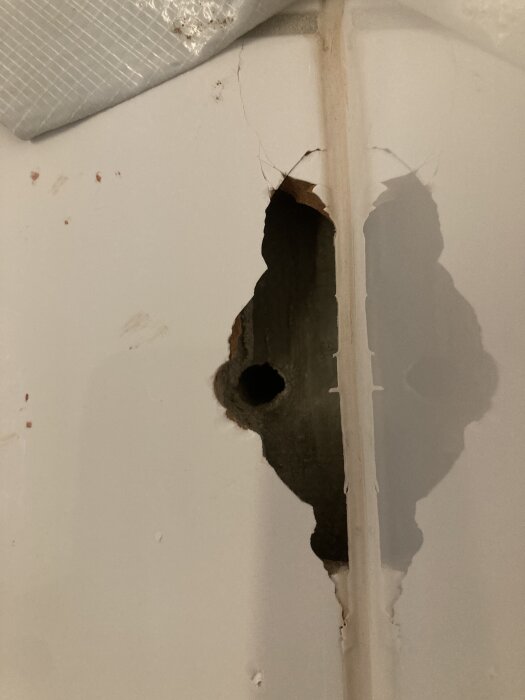 Sprucken kakelplatta i badrumsvägg med hål som exponerar tätskiktet bakom.