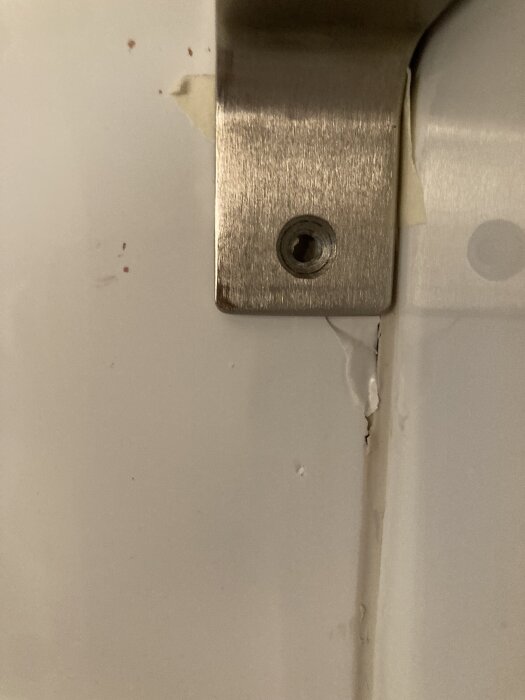 Närbild av en vägg med ett rostfritt stålfäste och synligt hål. Väggens yta är skadad med sprickor och färgavflagning runt fästet.