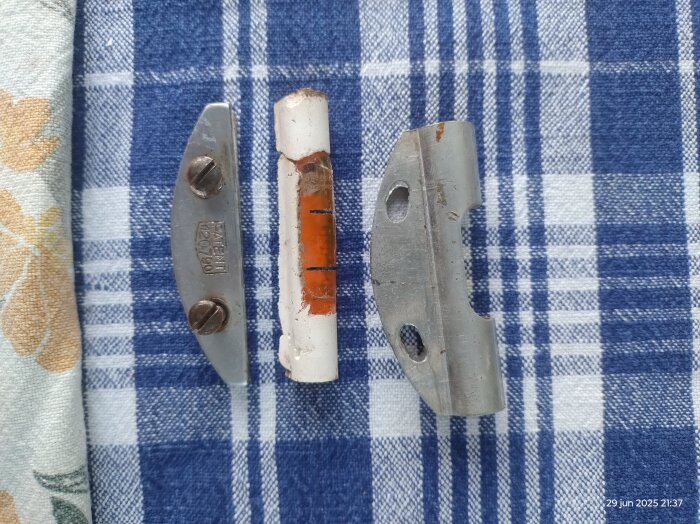 Delar av en gammal vattenpassampull med orange vätska, placerad på en blå- och vitrutigt tygbakgrund.