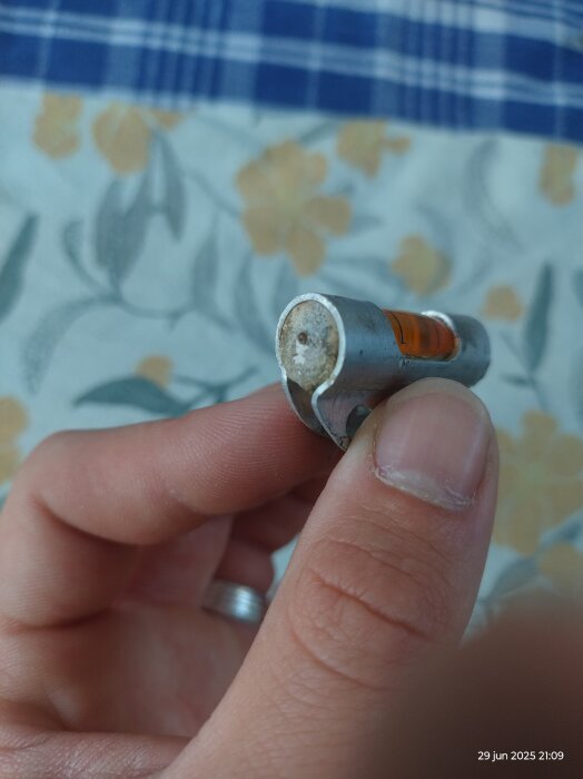 Närbild av en hand som håller en gammal vattenpassampull med orange vätska inuti, sannolikt från en Gustav Georg Carlsson vattenpass.