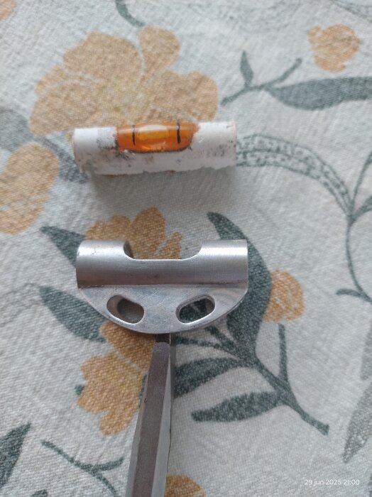 Gammal GGB vattenpassdel med orange ampull, omgiven av krita och metallverktyg på blommigt tygunderlag.