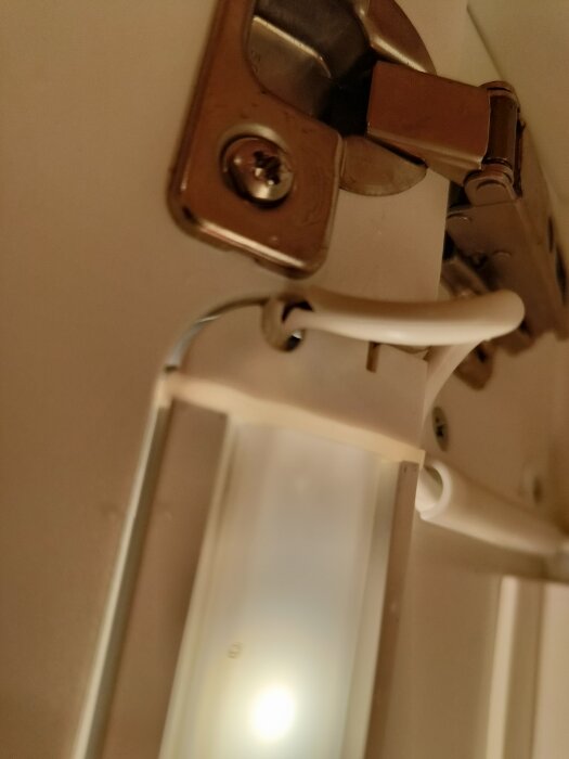 Skada på ledning i ett Ikea-badrumsskåp nära gångjärn, orsakande problem med den inbyggda belysningen.