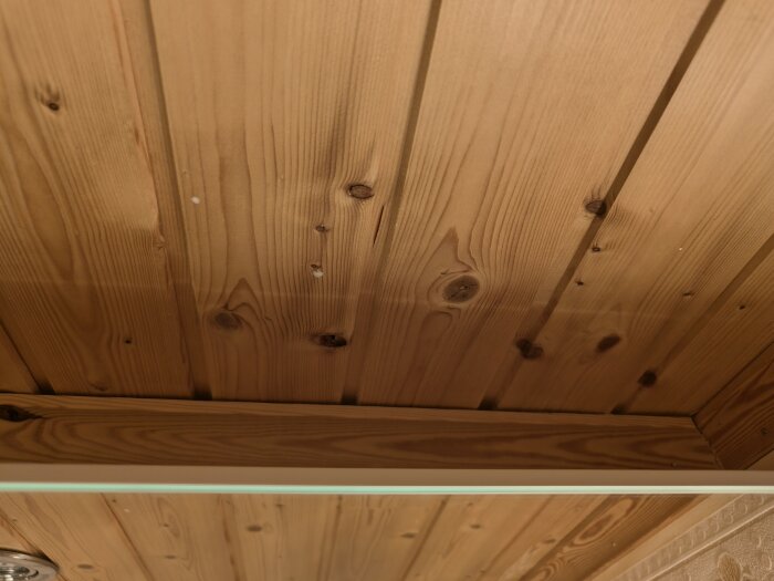 Trätak ovanför ett spegelskåp i ett badrum, detalj av träpanelens ådring och knutar synliga.