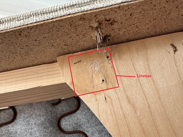 Träbit under soffa med markerade ytor för limning, visar spånskiva med stift som behöver tas bort.