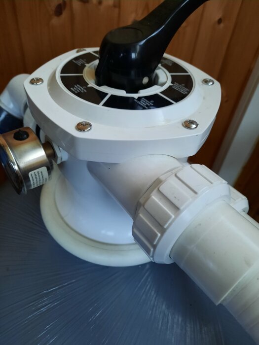 Poolfilter med vred och röranslutningar, tillverkat av Mega, monterat mot en trävägg.