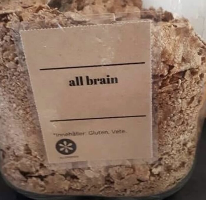 En burk med flingor märkt "all brain" med text om att innehålla gluten och vete, troligen serverad vid hotellfrukost.