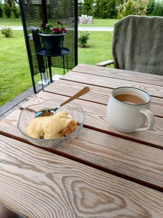 Vaniljsås och rabarberpaj i en skål på ett träbord utomhus, med en kopp te bredvid.