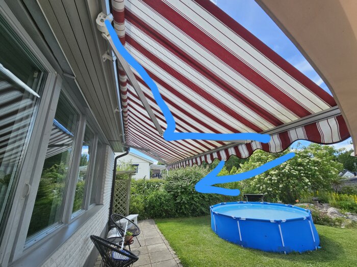 Markis över uteplats med blå pilar som pekar mot en arm, pool i bakgrunden.