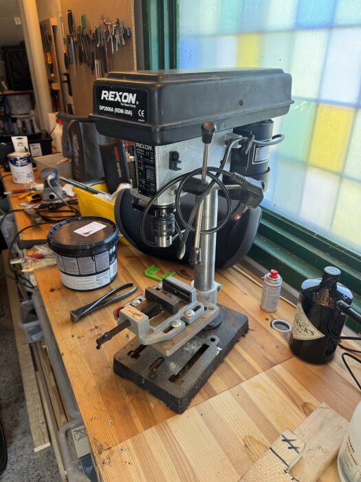 Begagnad bänkpelarborr, modell Rexon DP200A, placerad på en arbetsbänk i verkstadsmiljö med verktyg och material runtomkring.