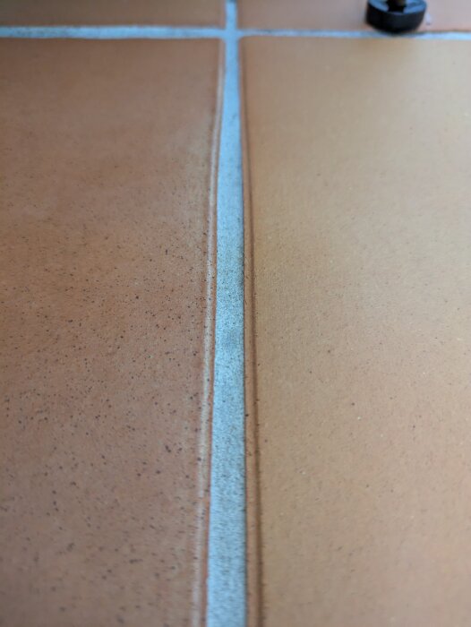 Närbild av rengjord fog mellan orangea kakelplattor.