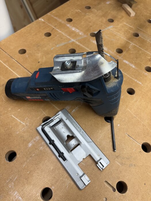 Multiverktyg med sågblad på arbetsbänk, med tillhörande tillbehör bredvid.