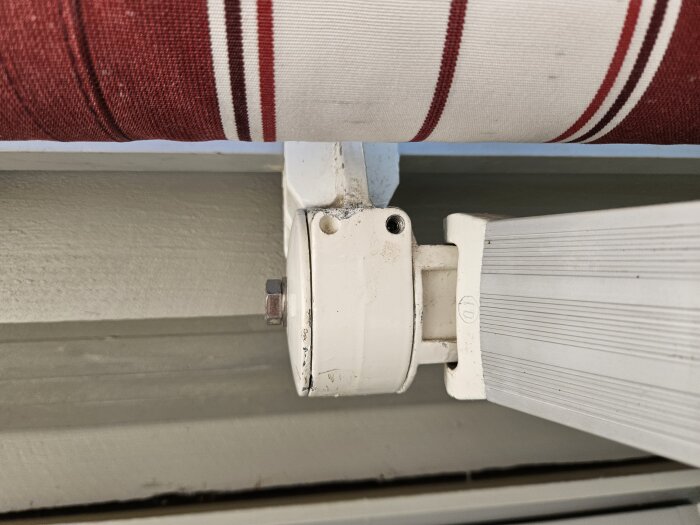 Rödvit randig markis som är fäst i en vit konsol på väggen, visar en del av mekanismen.