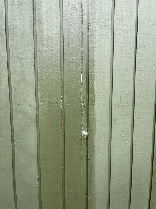 Grön husfasad med vertikala brädor, där vissa är i dåligt skick med sprickor och ojämn yta, utan uppmätta fuktproblem.