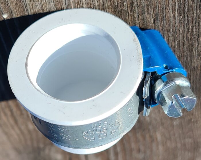 Slangnippelpropp med vit och blå komponent, monterad på en träbakgrund.