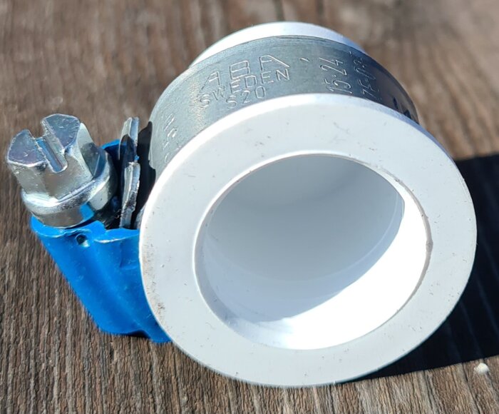 Slangnippelpropp i metall och plast med blå tätning och skruvklämma, ligger på trämaterial.