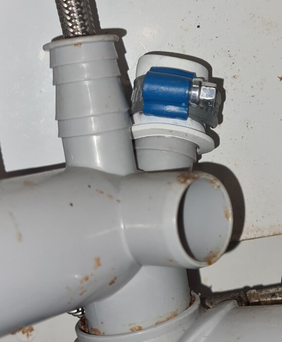 Grå plastslang med slangnippelpropp och blå metallklämma, del av avloppstillbehör, med några rostfläckar.