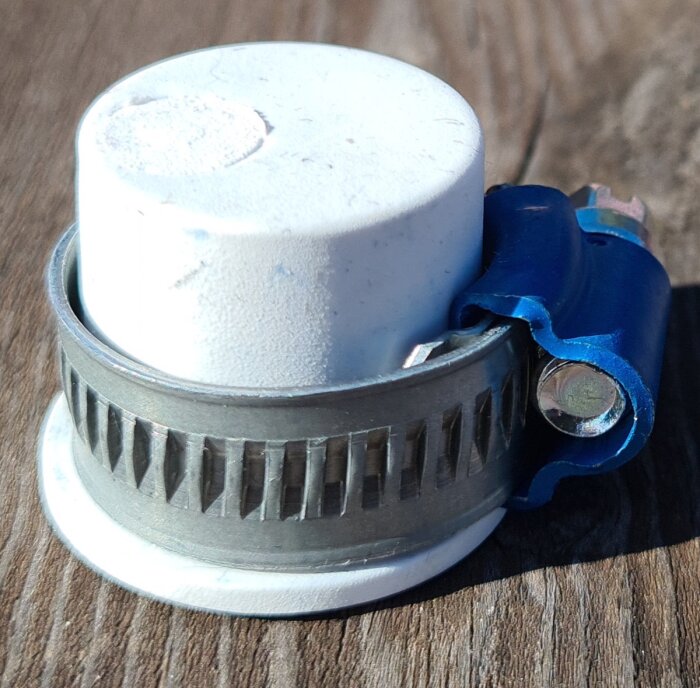 Slangnippelpropp med slangklämma på träbord.