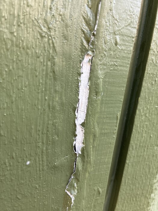 Sprucken grönmålad yta med synlig vit filler under färgen.