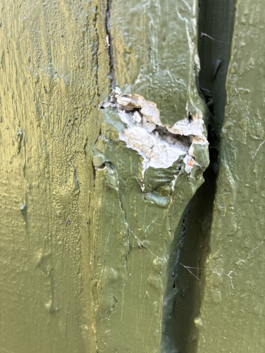 Grönmålad yta med spricka och exponerad filler.